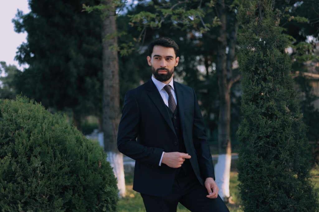 A sophisticated man in a suit posing confidently in a lush outdoor garden.
